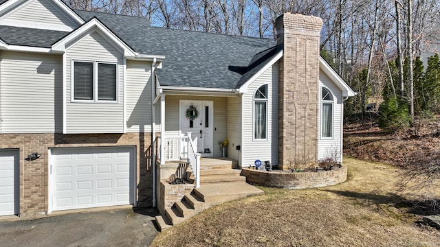 view of front of property with roof with shingles, an attached garage, a chimney, aphalt driveway, and brick siding