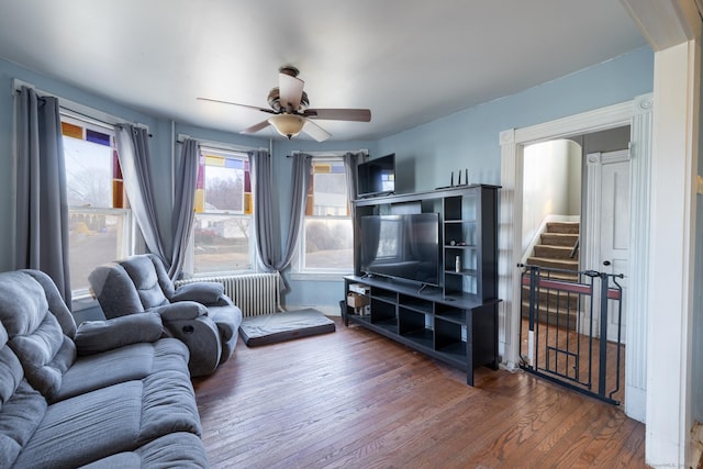 living room featuring ceiling fan, stairway, wood finished floors, and radiator heating unit