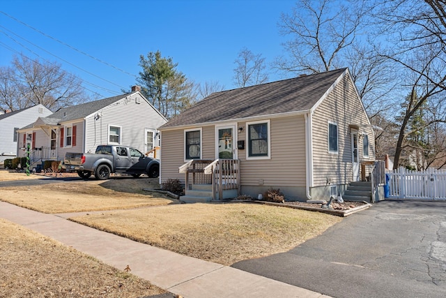 bungalow-style home featuring roof with shingles, a front yard, and fence