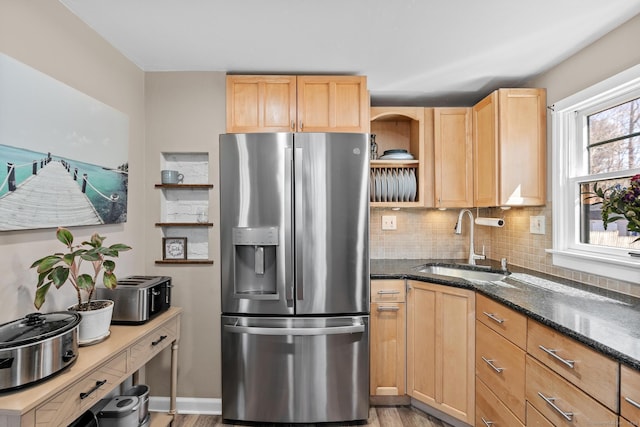 kitchen featuring light brown cabinetry, stainless steel refrigerator with ice dispenser, a sink, dark stone countertops, and decorative backsplash