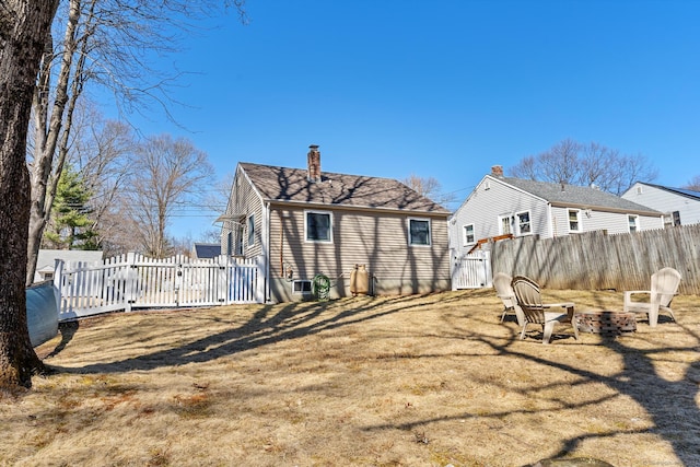 back of property with a chimney, a lawn, a fire pit, and fence