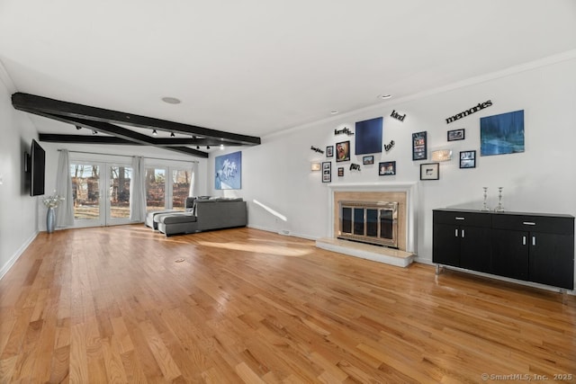 unfurnished living room with baseboards, beamed ceiling, light wood-type flooring, ornamental molding, and a glass covered fireplace