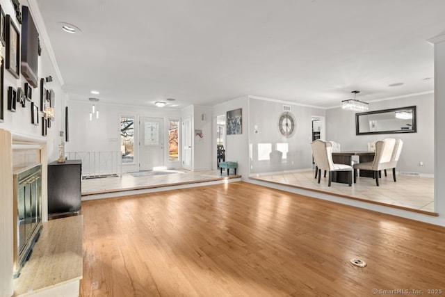 unfurnished living room featuring crown molding, baseboards, a fireplace, an inviting chandelier, and wood finished floors