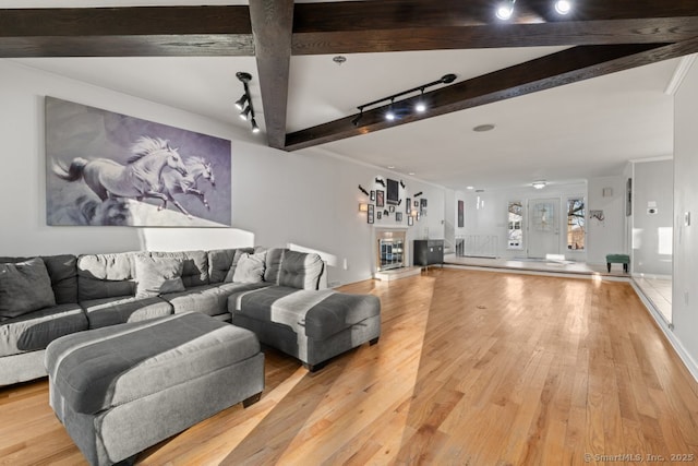 living room featuring a tiled fireplace, beam ceiling, rail lighting, and light wood-type flooring