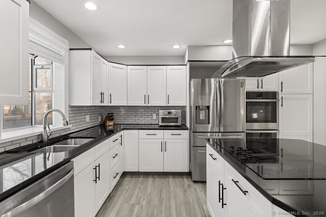 kitchen featuring decorative backsplash, stainless steel appliances, island range hood, white cabinetry, and a sink