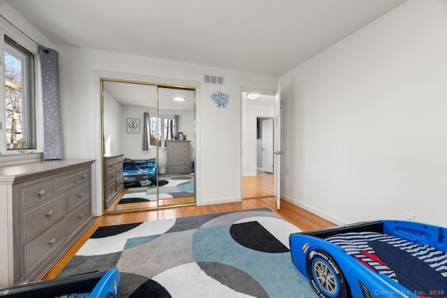 bedroom with a closet, visible vents, light wood-type flooring, and baseboards