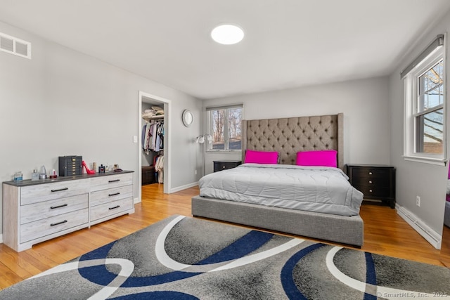 bedroom featuring visible vents, multiple windows, a walk in closet, and wood finished floors