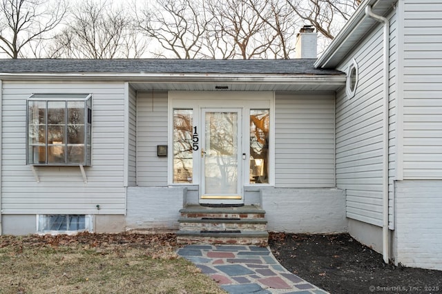 view of exterior entry featuring a chimney and a shingled roof