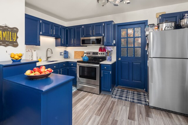 kitchen featuring blue cabinets, light wood-type flooring, a sink, stainless steel appliances, and light countertops