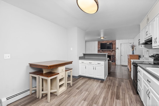 kitchen with light wood finished floors, black range with electric stovetop, under cabinet range hood, white cabinetry, and a baseboard radiator