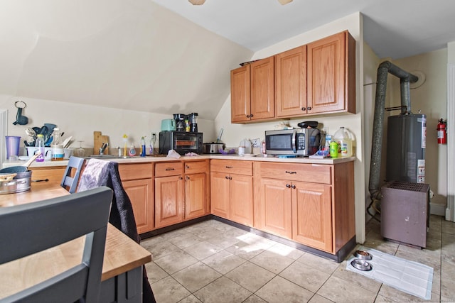 kitchen featuring stainless steel microwave, gas water heater, light countertops, lofted ceiling, and a sink