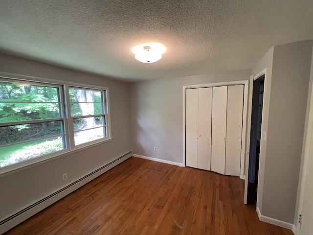 unfurnished bedroom featuring wood finished floors, a closet, baseboard heating, and baseboards