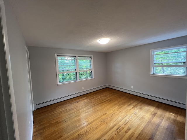 unfurnished room featuring baseboard heating, wood finished floors, a wealth of natural light, and a textured ceiling