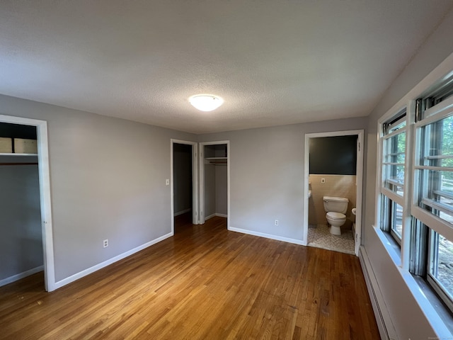 unfurnished bedroom featuring baseboards, multiple closets, ensuite bathroom, light wood-style floors, and a textured ceiling