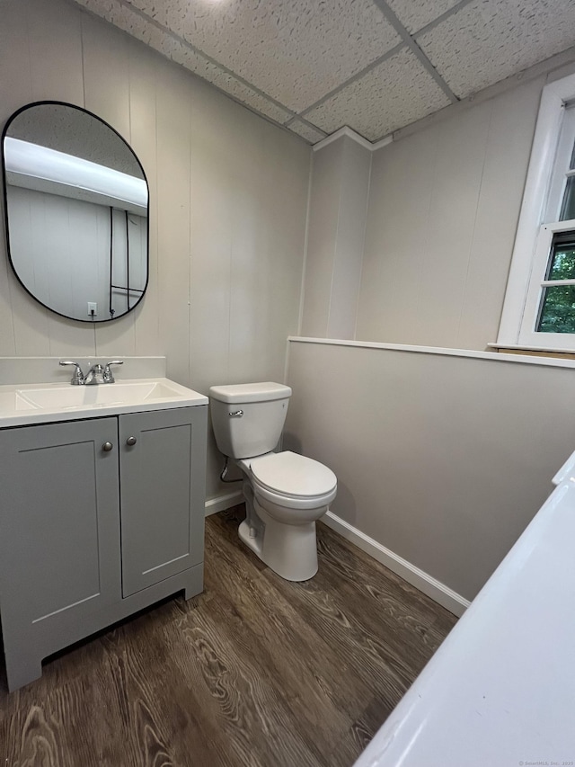 bathroom featuring baseboards, a drop ceiling, toilet, wood finished floors, and vanity