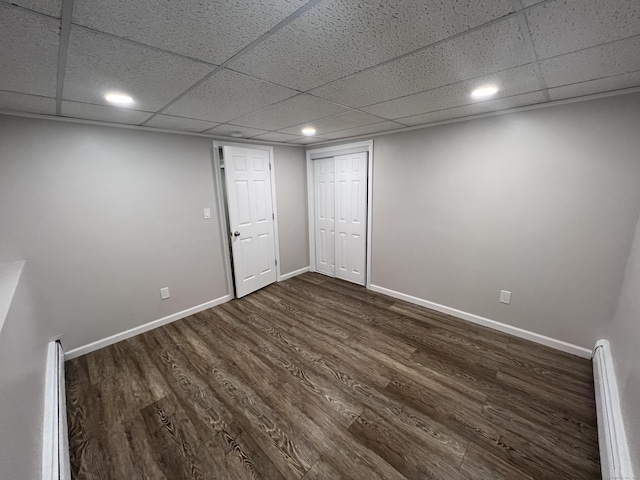 interior space featuring a baseboard radiator, a paneled ceiling, baseboards, and dark wood-style flooring