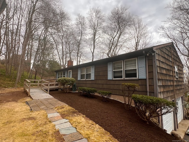 view of side of property featuring a wooden deck, an attached garage, and a chimney