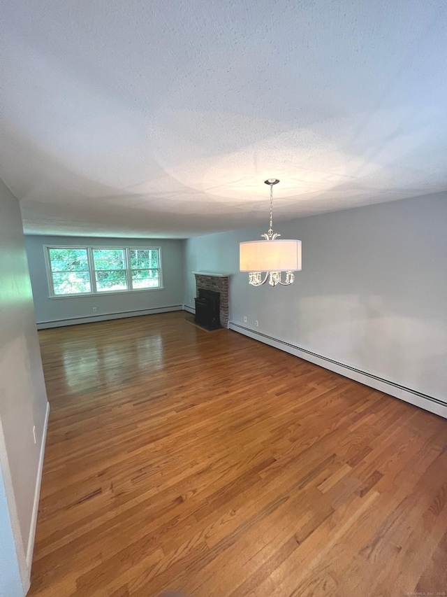 interior space featuring a brick fireplace, baseboards, a chandelier, baseboard heating, and wood finished floors