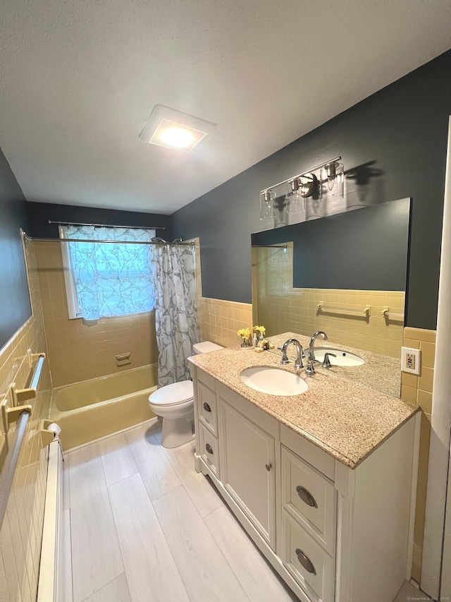 bathroom with vanity, shower / bathtub combination with curtain, wainscoting, tile walls, and toilet