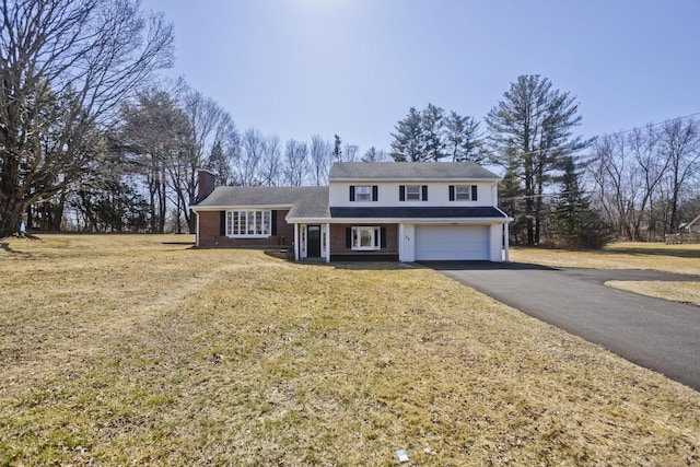 traditional-style home featuring a front yard, a chimney, a garage, aphalt driveway, and brick siding