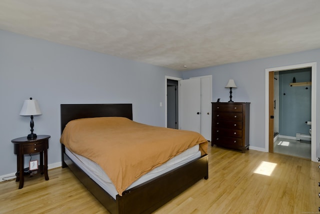 bedroom with a baseboard heating unit, light wood-style flooring, and baseboards