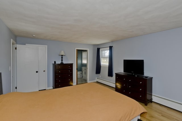 unfurnished bedroom with a closet, light wood-type flooring, baseboard heating, and connected bathroom