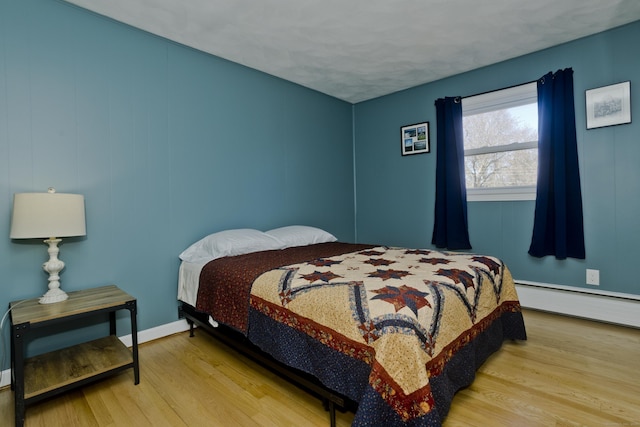 bedroom with a baseboard heating unit, wood finished floors, and baseboards