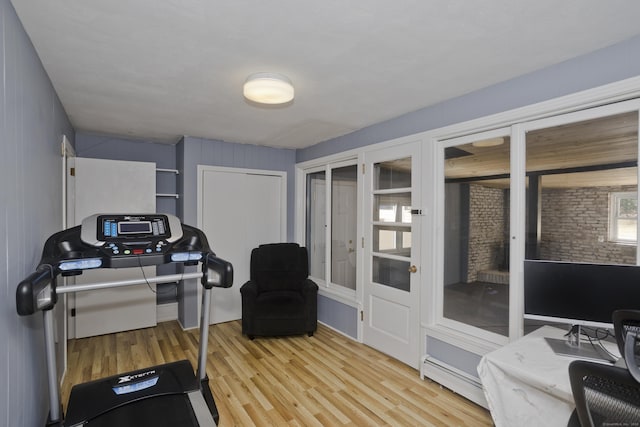 exercise room featuring a baseboard heating unit and light wood finished floors