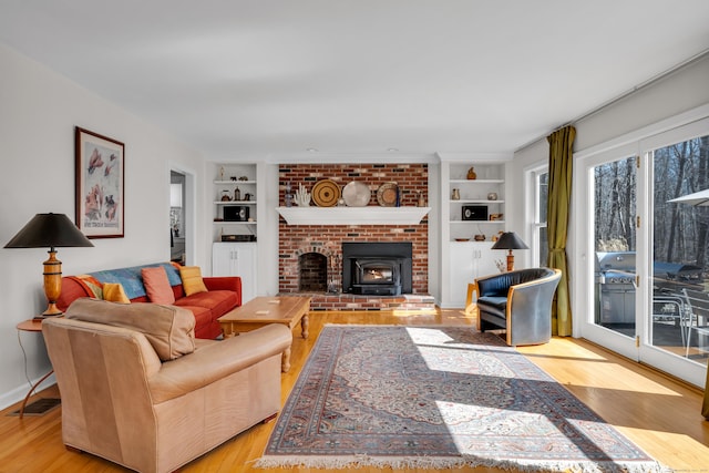 living area with visible vents, a brick fireplace, built in shelves, and wood finished floors