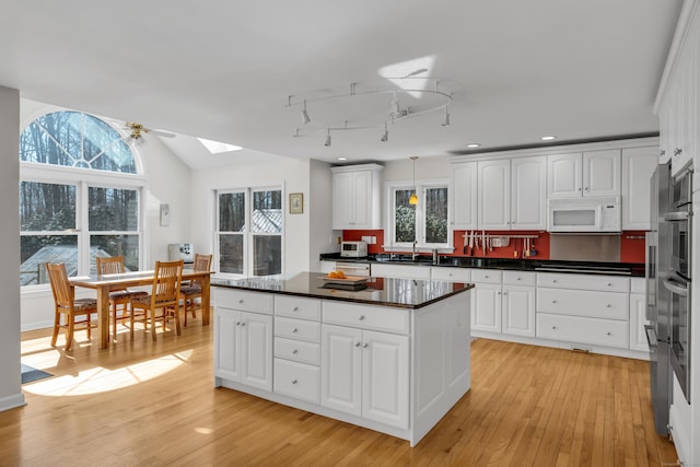 kitchen with lofted ceiling with skylight, light wood-style flooring, a sink, dark countertops, and white microwave