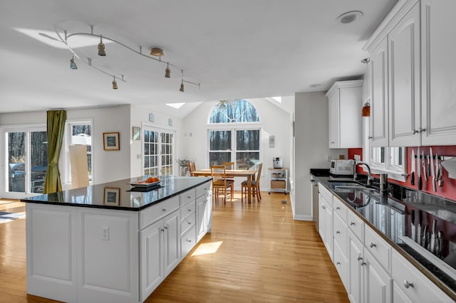 kitchen featuring a sink, light wood-style floors, lofted ceiling with skylight, and dark countertops