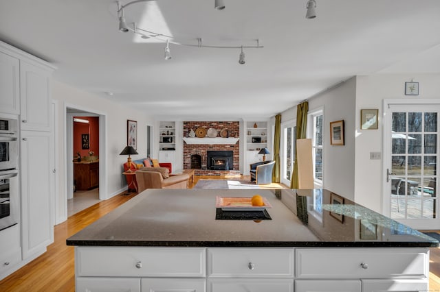 kitchen featuring built in features, a kitchen island, dark stone counters, light wood-style flooring, and white cabinets