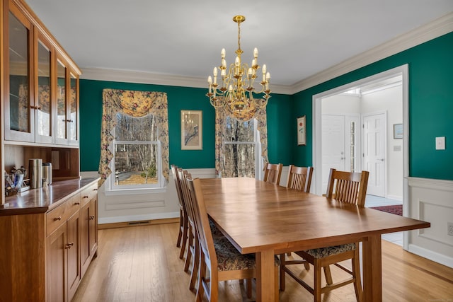 dining room featuring a chandelier, light wood-style flooring, wainscoting, and ornamental molding