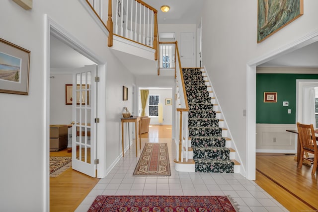 entrance foyer featuring tile patterned flooring, a wainscoted wall, a towering ceiling, and ornamental molding