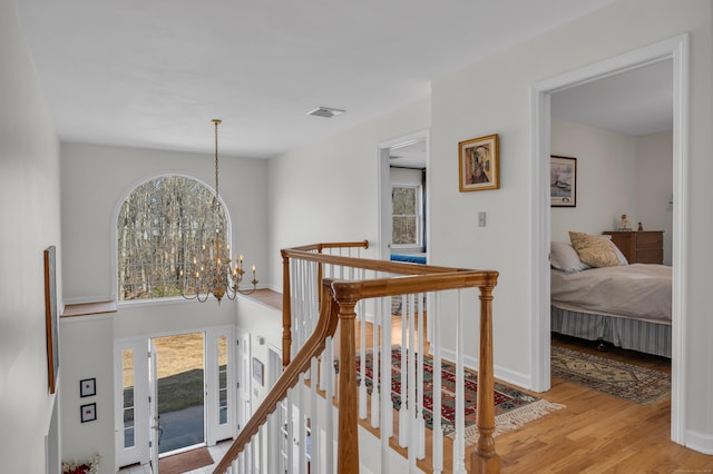 hallway featuring visible vents, an upstairs landing, light wood-style flooring, baseboards, and a chandelier