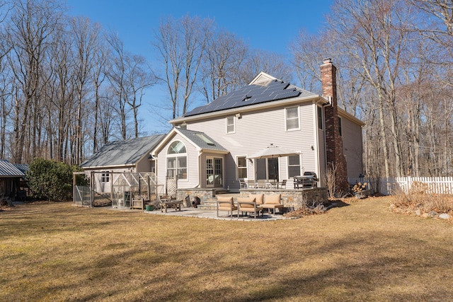 back of property featuring a lawn, a patio, roof mounted solar panels, an outdoor hangout area, and a chimney