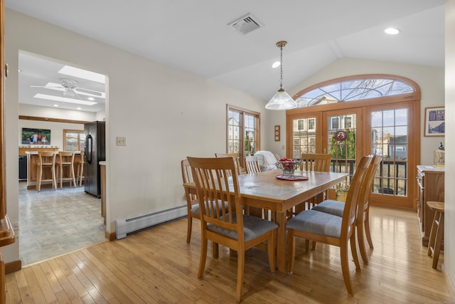 dining area featuring visible vents, a baseboard radiator, vaulted ceiling with skylight, french doors, and light wood-type flooring