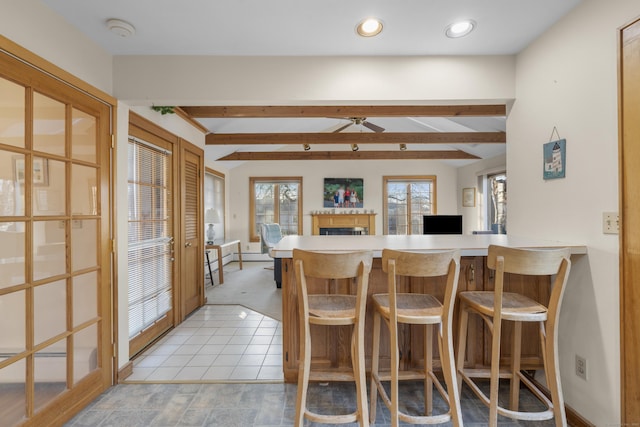 kitchen with vaulted ceiling with beams, a kitchen breakfast bar, a peninsula, a ceiling fan, and a baseboard radiator