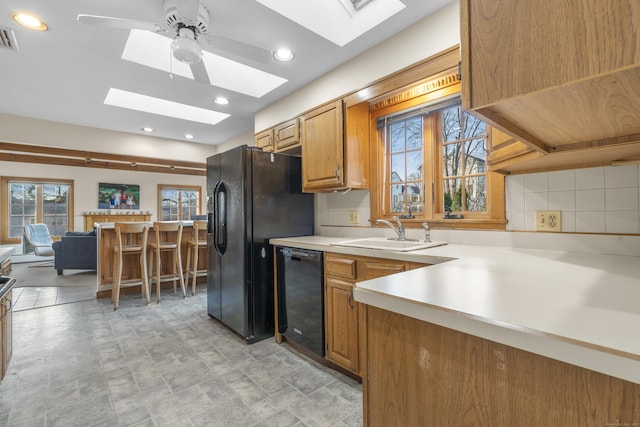 kitchen with a skylight, a sink, black appliances, light countertops, and tasteful backsplash