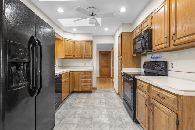 kitchen featuring a skylight, ceiling fan, black appliances, light countertops, and brown cabinets