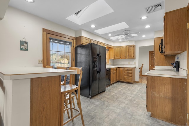 kitchen with visible vents, a kitchen bar, black appliances, a peninsula, and a skylight