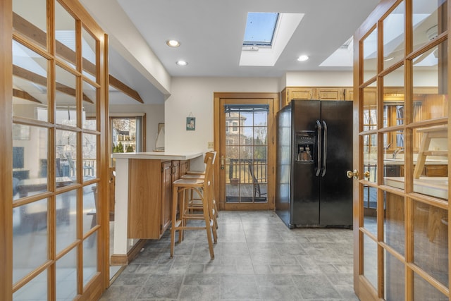 kitchen featuring a breakfast bar area, light countertops, recessed lighting, black fridge, and a peninsula