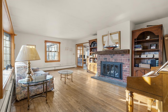 living area featuring light wood finished floors, visible vents, a brick fireplace, and a baseboard heating unit