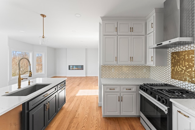 kitchen featuring tasteful backsplash, wall chimney range hood, light wood-style flooring, gas stove, and a sink