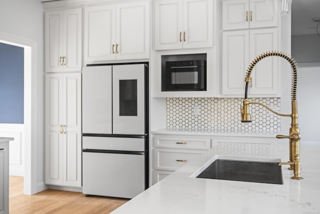 kitchen with light stone counters, a sink, light wood-style floors, white cabinetry, and refrigerator with glass door