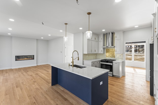 kitchen featuring a sink, a glass covered fireplace, wall chimney range hood, decorative backsplash, and gas range