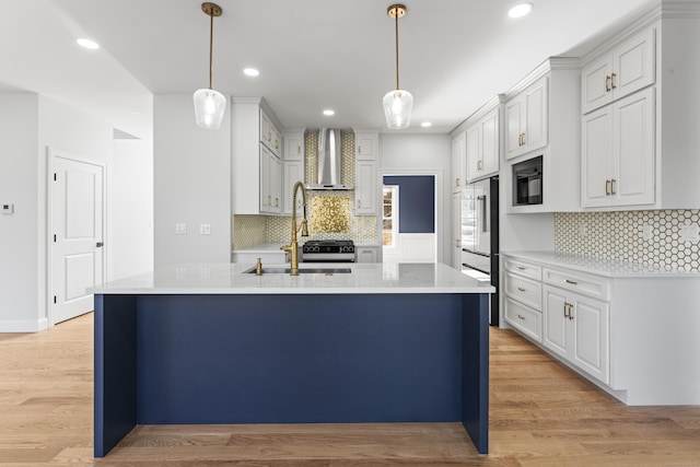 kitchen featuring light countertops, light wood-style floors, wall chimney range hood, and a sink