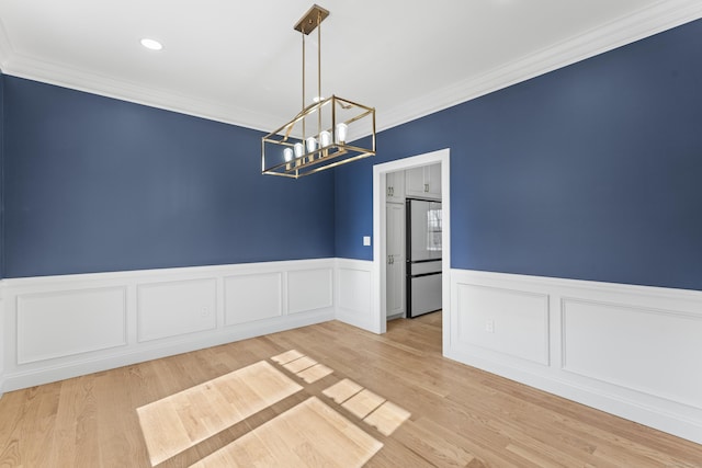 unfurnished room featuring a chandelier, a wainscoted wall, crown molding, and wood finished floors