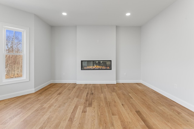 unfurnished living room with a glass covered fireplace, recessed lighting, baseboards, and wood finished floors