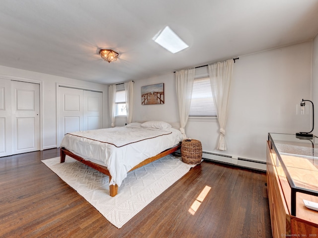 bedroom with dark wood-type flooring, baseboard heating, and multiple closets